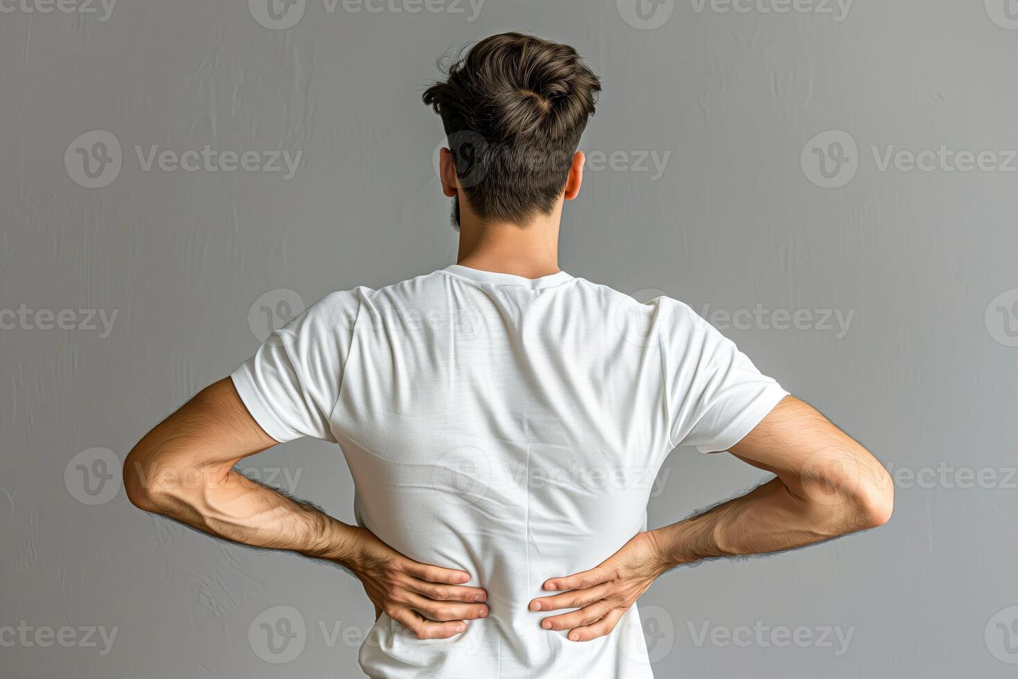 Man with back pain standing against a gray wall photo