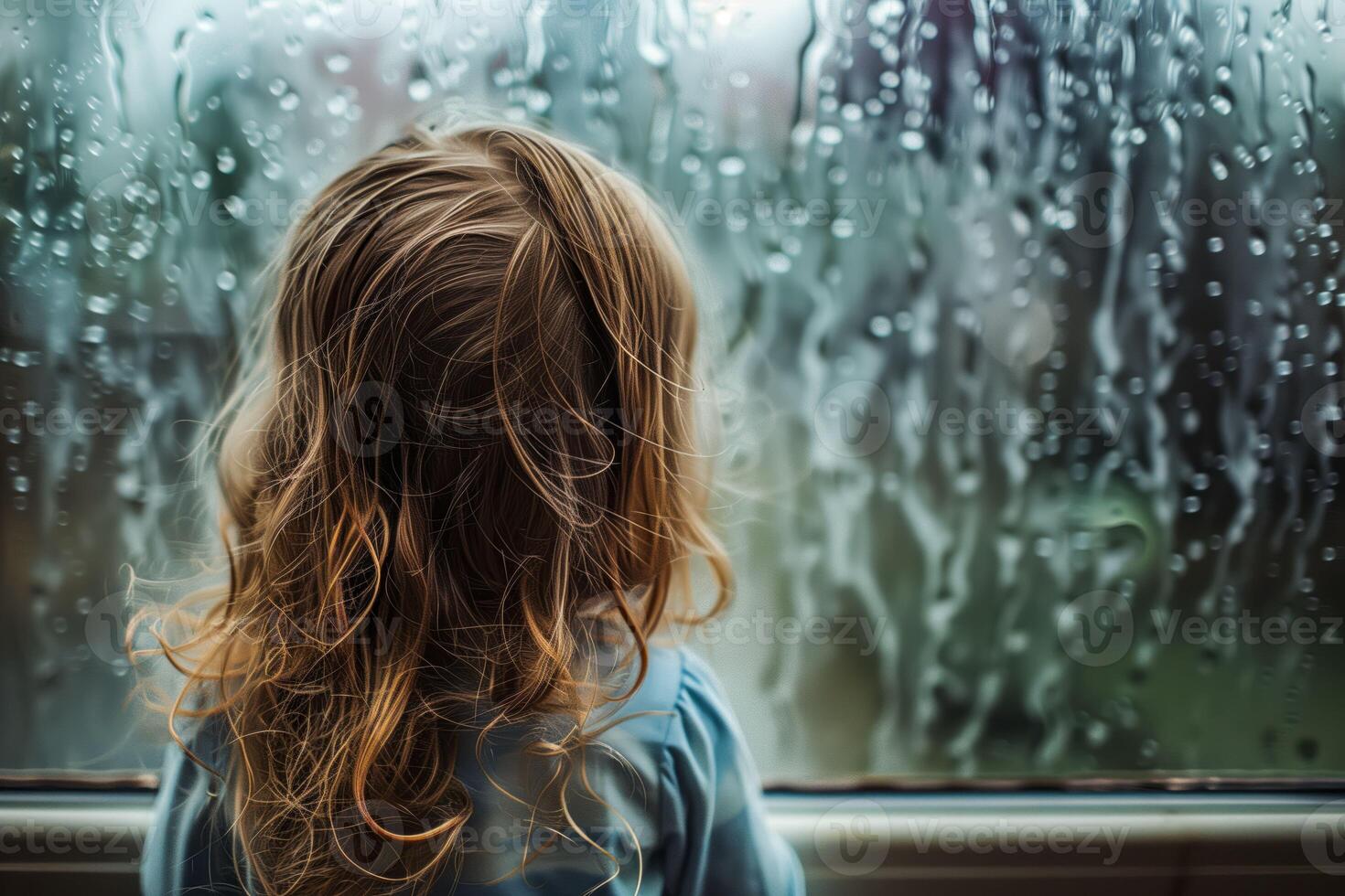Child observing rain drops through window photo