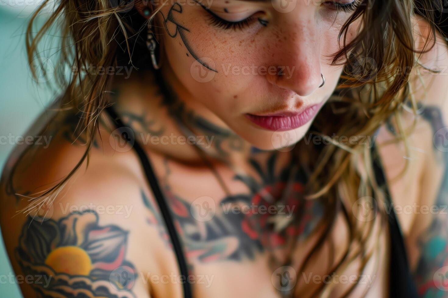 Woman with tattoos on her arms and chest looking down photo