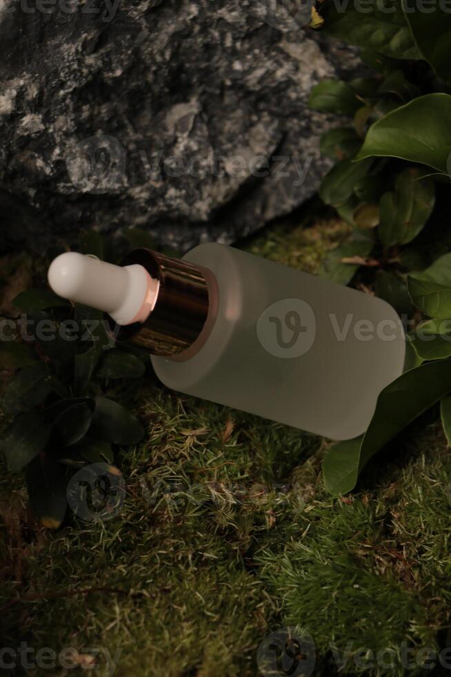 Frosted Dropper Bottle with Rose Gold Cap on Moss and Leafy Background photo