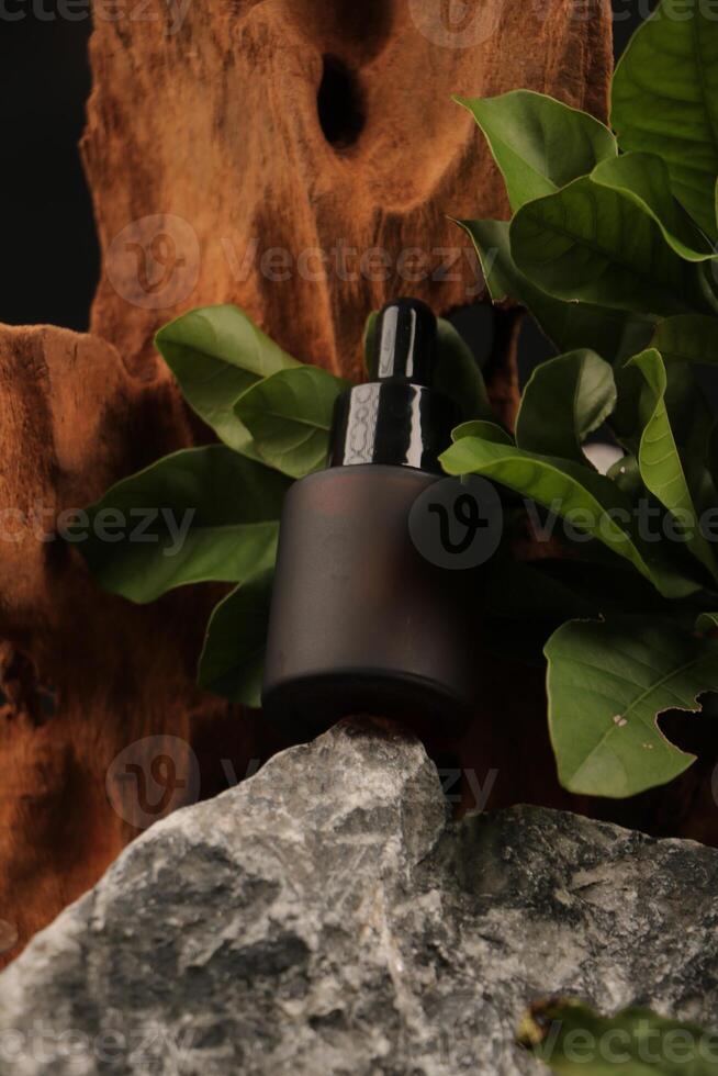 Matte Amber Dropper Bottle with Black Cap on Wood and Leaf Background photo
