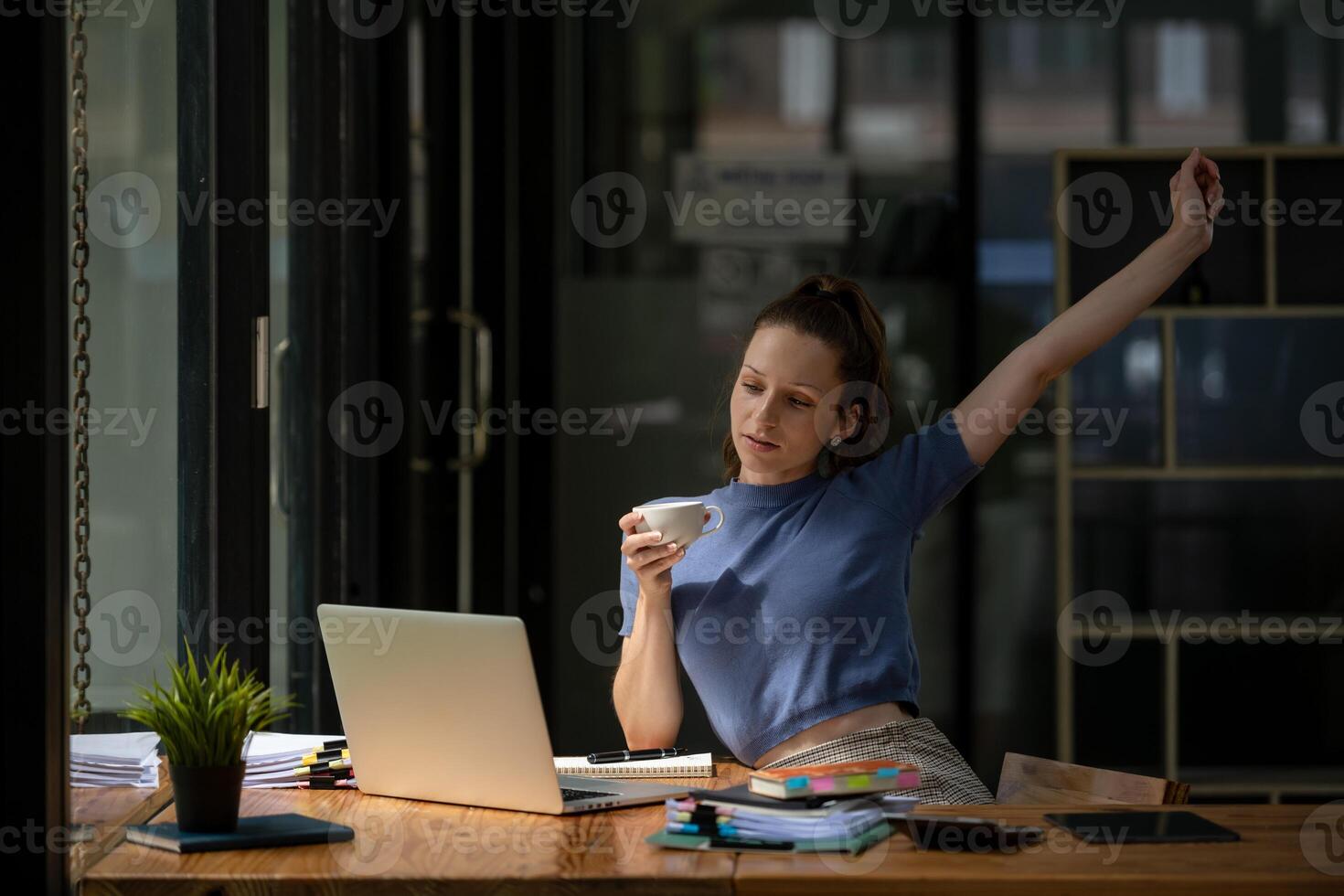 Businesswoman stretching lazy at the desk to relax while take a break from work and enjoy with coffee in the office. Feeling stressed and achy from work. photo