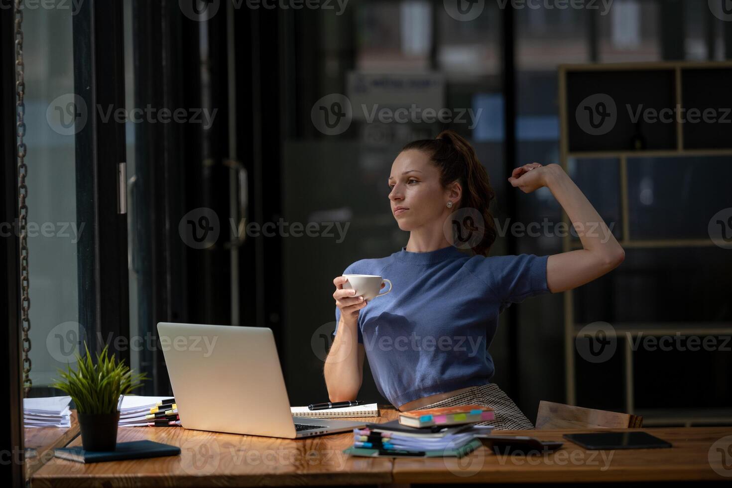Businesswoman stretching lazy at the desk to relax while take a break from work and enjoy with coffee in the office. Feeling stressed and achy from work. photo