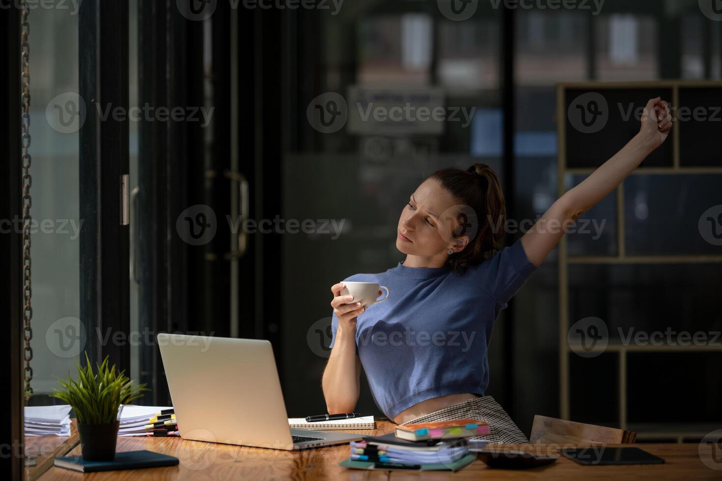 Businesswoman stretching lazy at the desk to relax while take a break from work and enjoy with coffee in the office. Feeling stressed and achy from work. photo