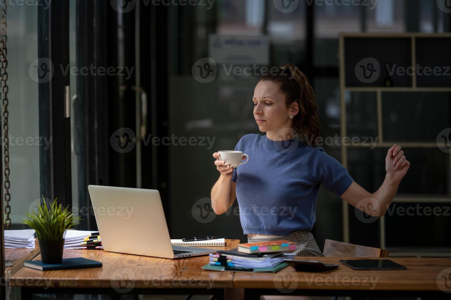 Businesswoman stretching lazy at the desk to relax while take a break from work and enjoy with coffee in the office. Feeling stressed and achy from work. photo