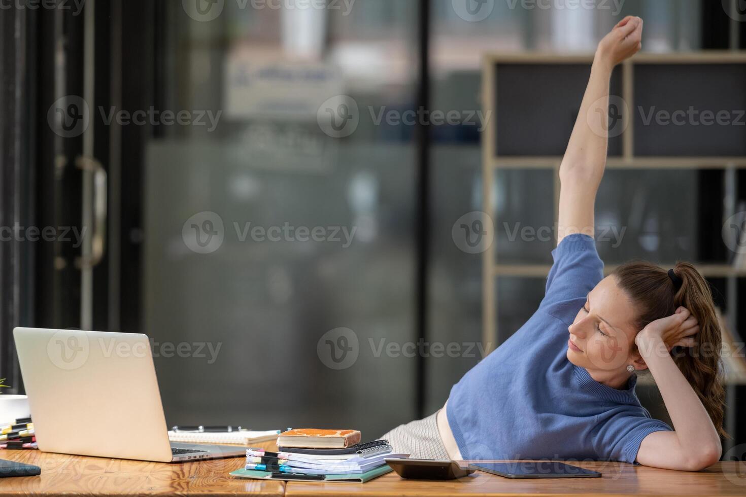 Businesswoman stretching lazy at the desk to relax while working in the office. Feeling stressed and achy from work. photo