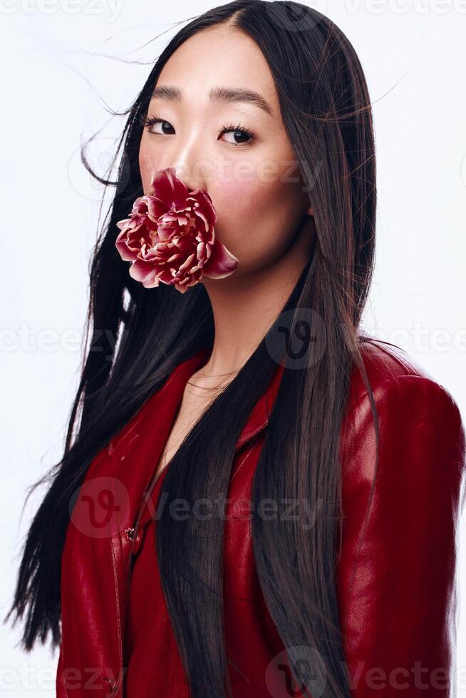 Mysterious woman with long black hair in red jacket holding a flower in her mouth photo