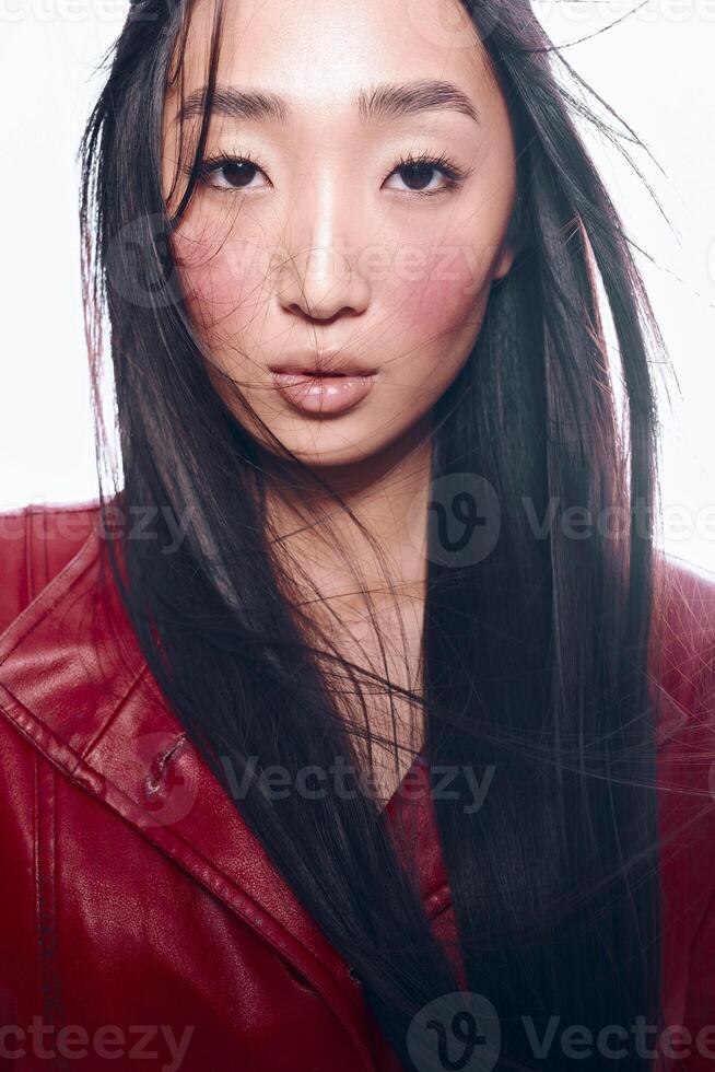 Portrait of a confident Asian woman with long black hair and a red jacket posing for the camera photo
