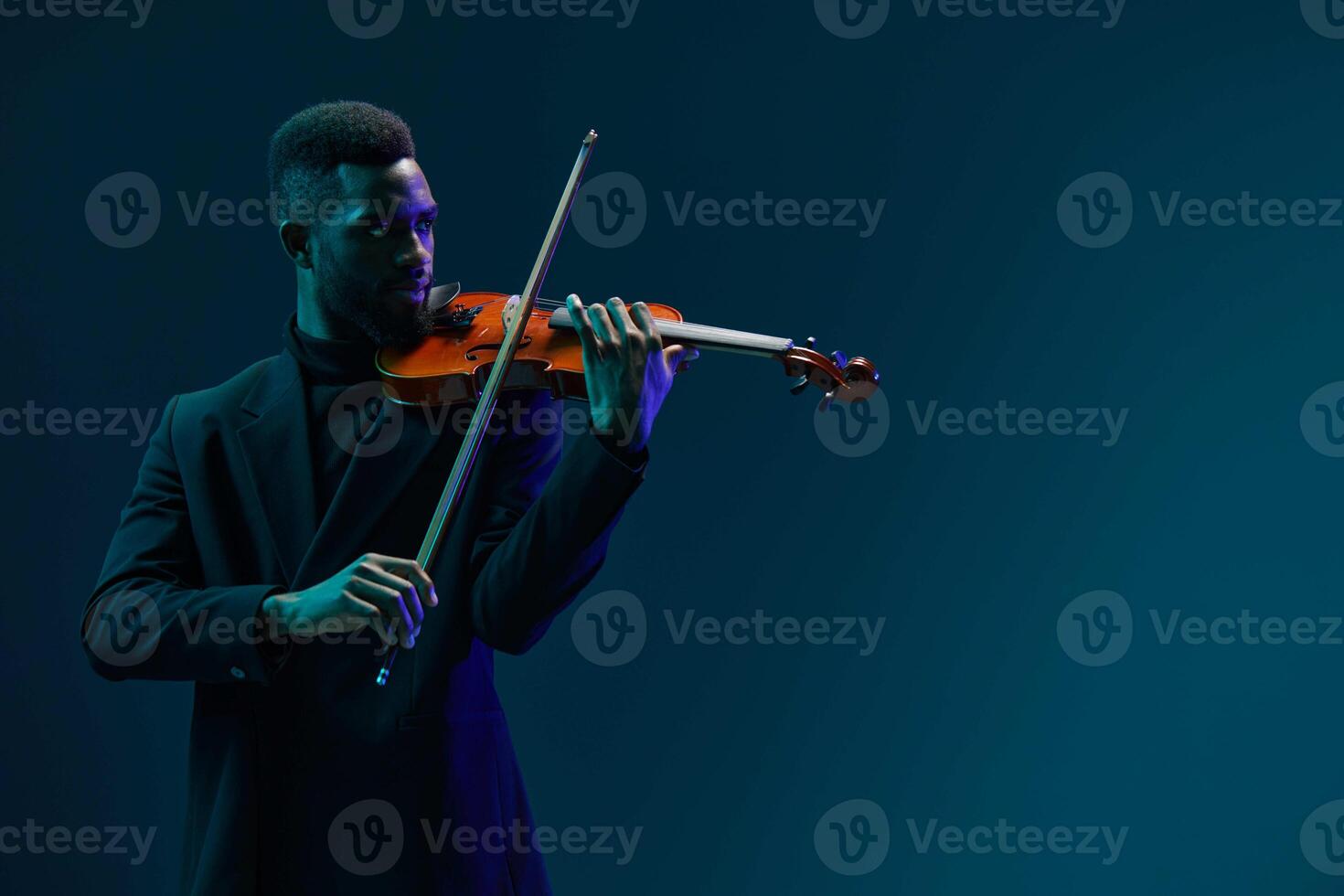 Talented young African American man playing violin on dark blue background with copy space photo