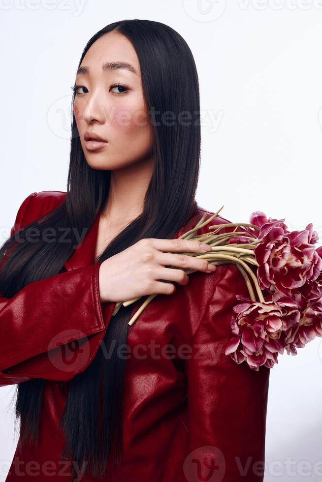 Stylish Asian woman in red leather jacket holding bouquet of pink flowers in urban setting photo