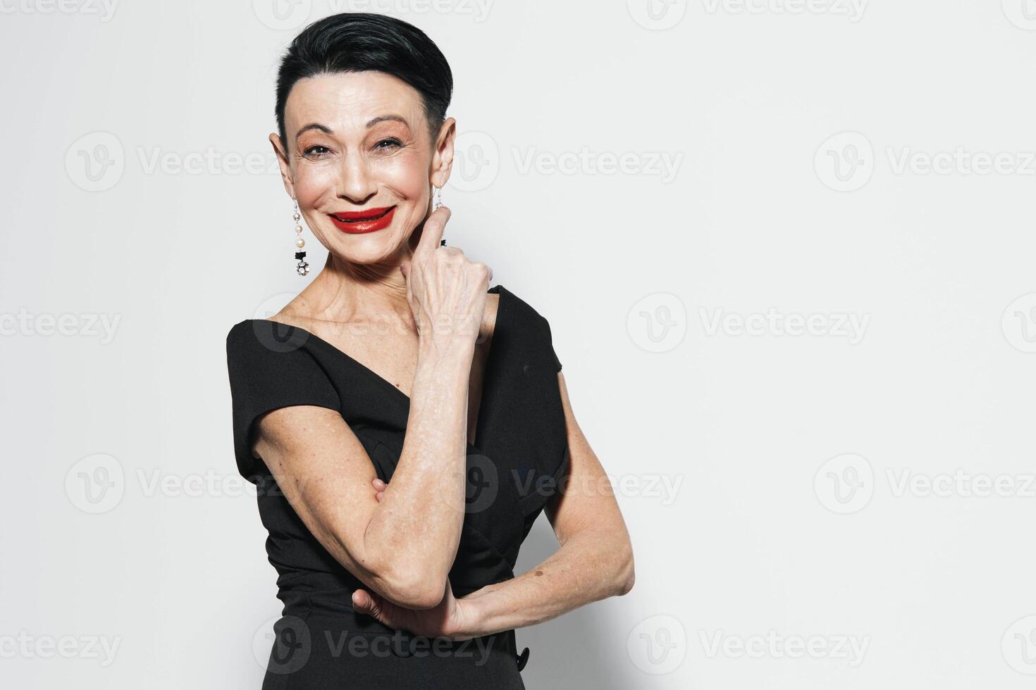 Elegant mature woman in stylish black dress and bold red lipstick posing gracefully against white photo