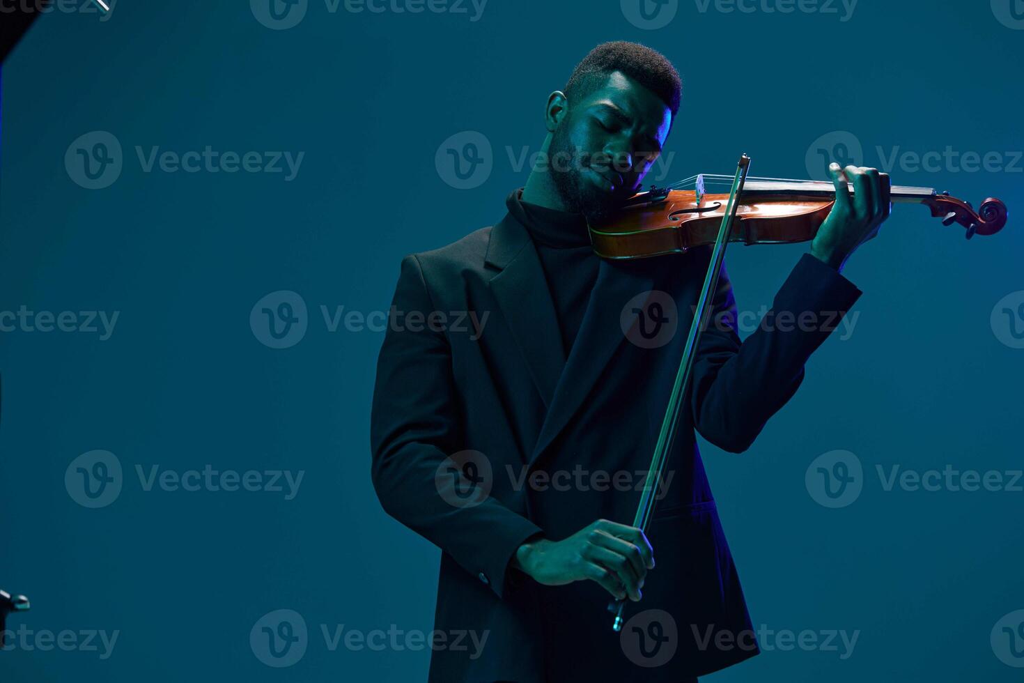 Elegant man in suit performing on violin in front of blue illuminated background for music concept photo
