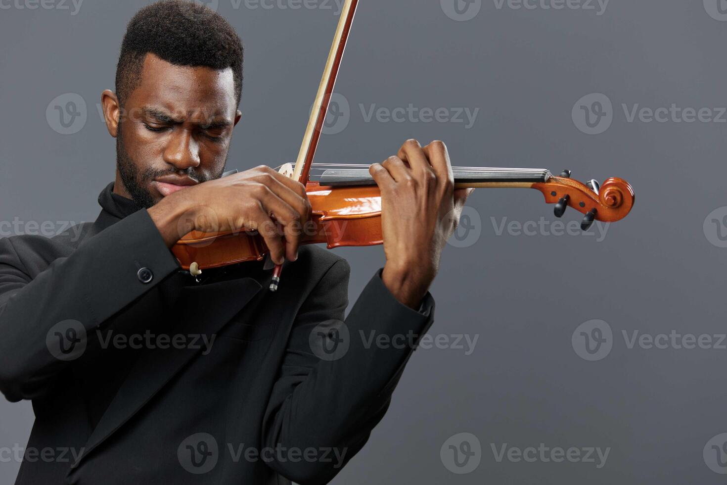 African American man in black suit playing violin on gray background in elegant music performance photo