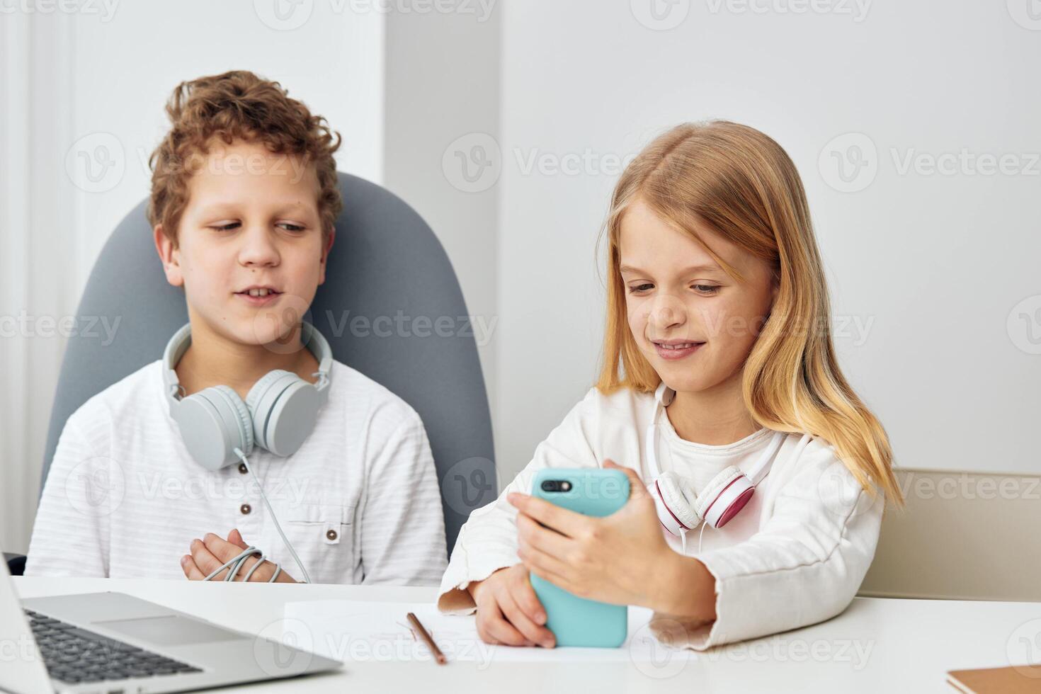 Happy children studying at home using laptops and tablets for elearning, sitting at a table in their photo