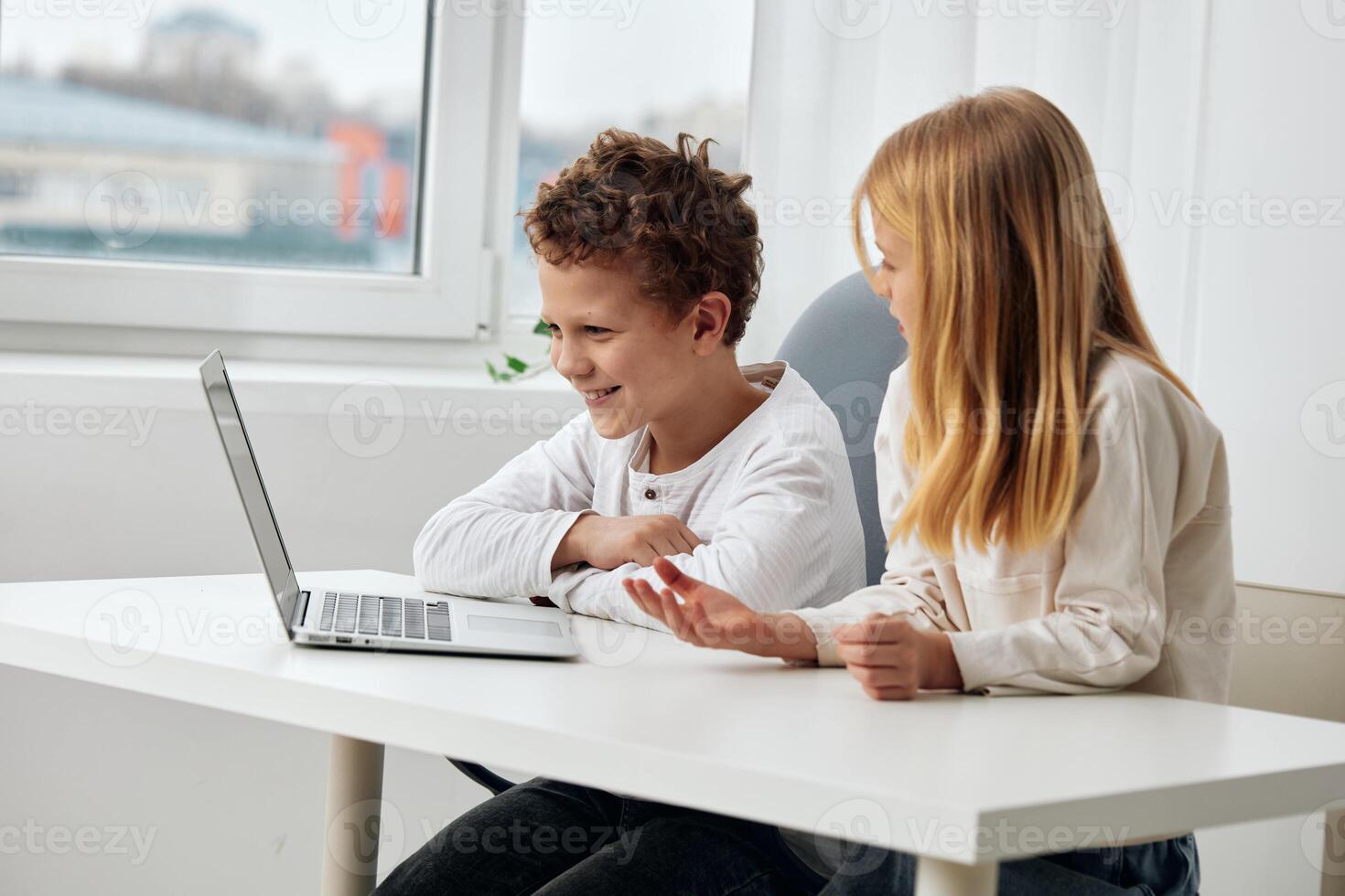 Happy Caucasian children sitting at a table in their cozy living room, engrossed in their online photo