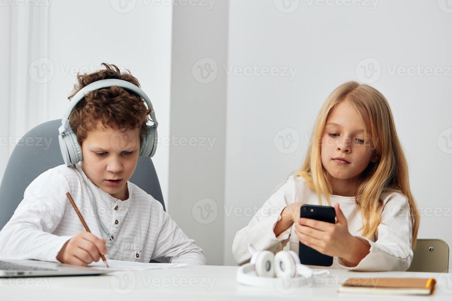 Happy siblings learning together at home using laptops and headphones They are sitting at a table in photo