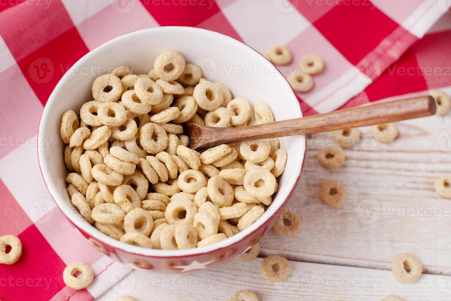 healthy cereal rings on a light wood background with tablecloth red in a plate and scattered on the table with sun rays. morning eat. Healthy children's breakfast. Dry muesli. photo