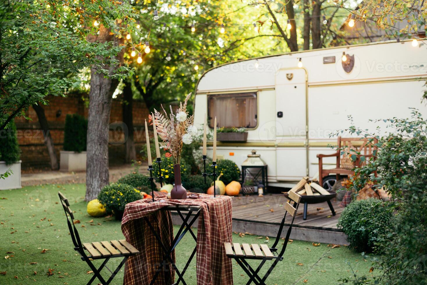Autumn evening, romantic dinner in the garden. Table with tablecloth and decoration. Trailer with autumn decor and light bulbs photo