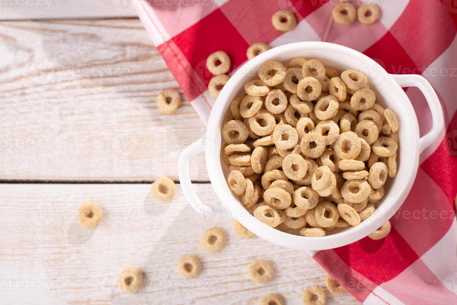 healthy cereal rings on a light wood background with tablecloth red in a plate and scattered on the table with sun rays. morning eat. Healthy children's breakfast. Dry muesli. photo