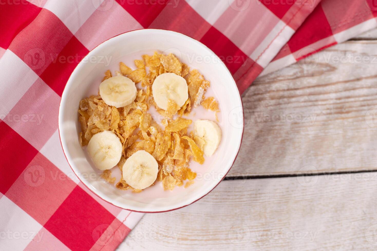 Healthy breakfast. Muesli with yogurt and banana on a light wooden background with a red tablecloth. View from above. Copy space. photo