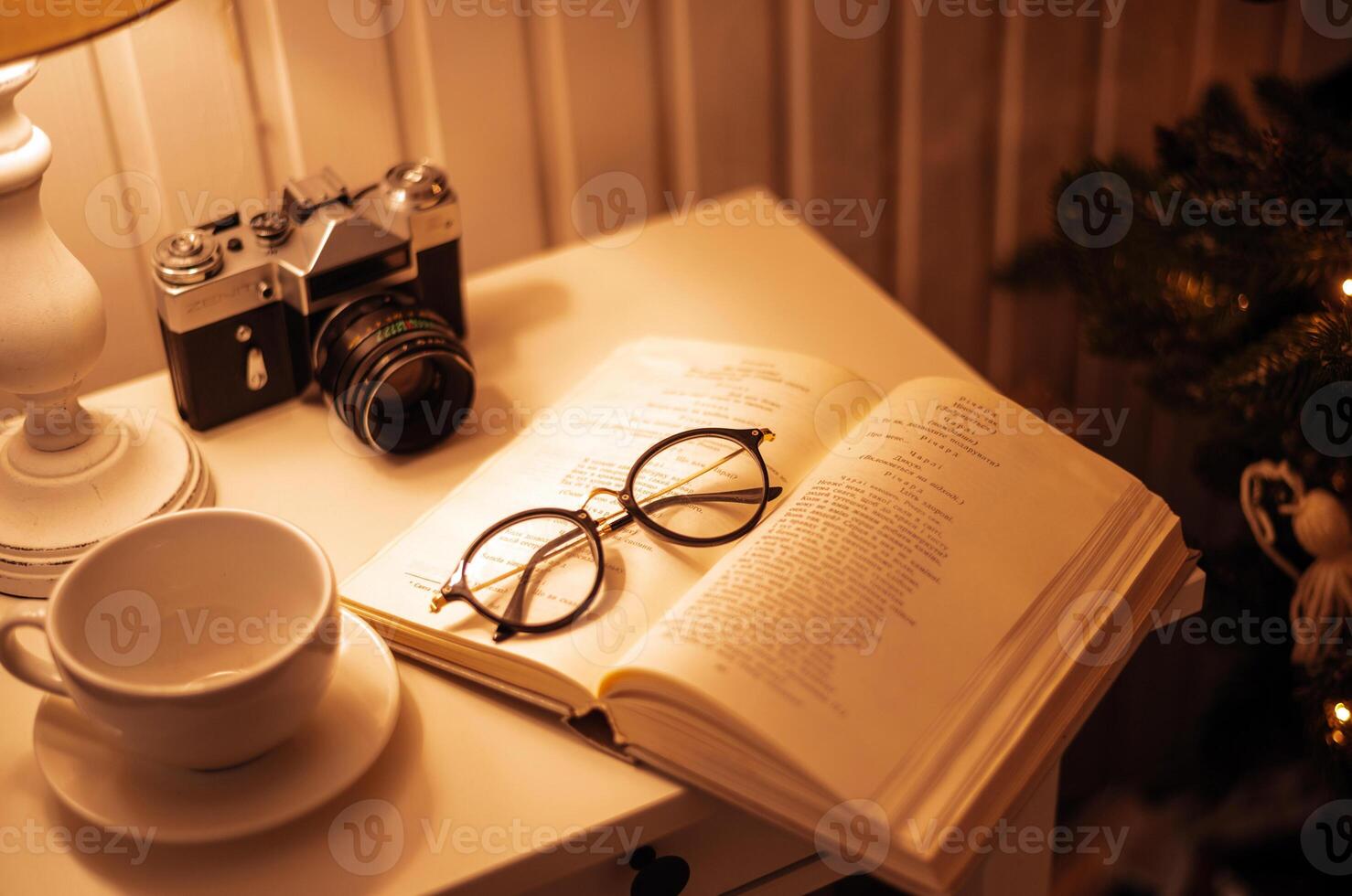 November 28, 2020. Kyiv, Ukraine. Vintage home atmosphere. Retro photo camera, glasses, coffee cup and book on the table with lamp. Selective focus