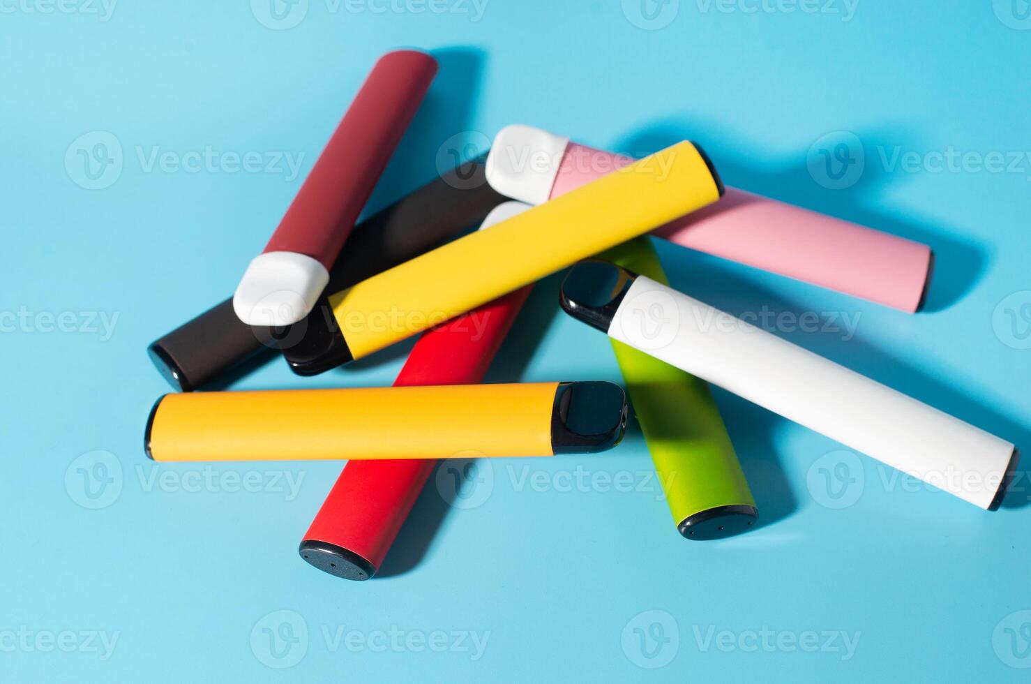 Layout of colorful disposable electronic cigarettes with shadows on a blue background. The concept of modern smoking, vaping and nicotine. Top view photo