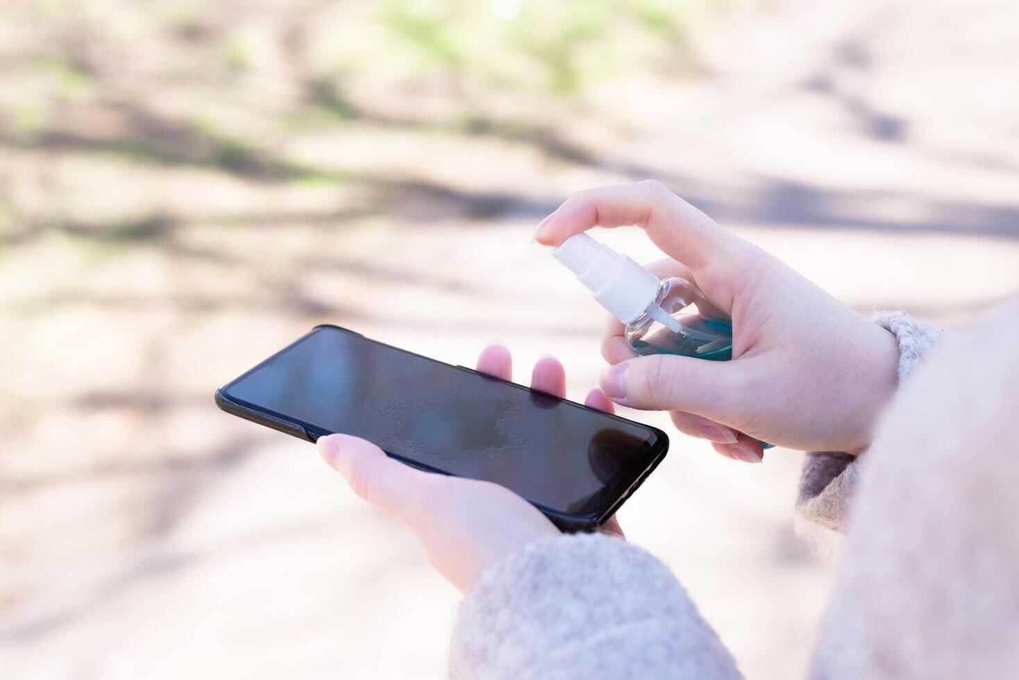 How to clean, sanitize your phone. Cleaning mobile phone to eliminate germs, coronavirus Covid-19. Man hands cleaning smartphone by disinfectant spray.Hygiene concept. photo