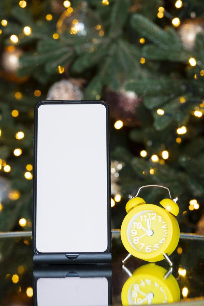 Phone with isolated screen and clock alarm on the background of the Christmas tree, bokeh and garland. New year gift, sales and offers. photo