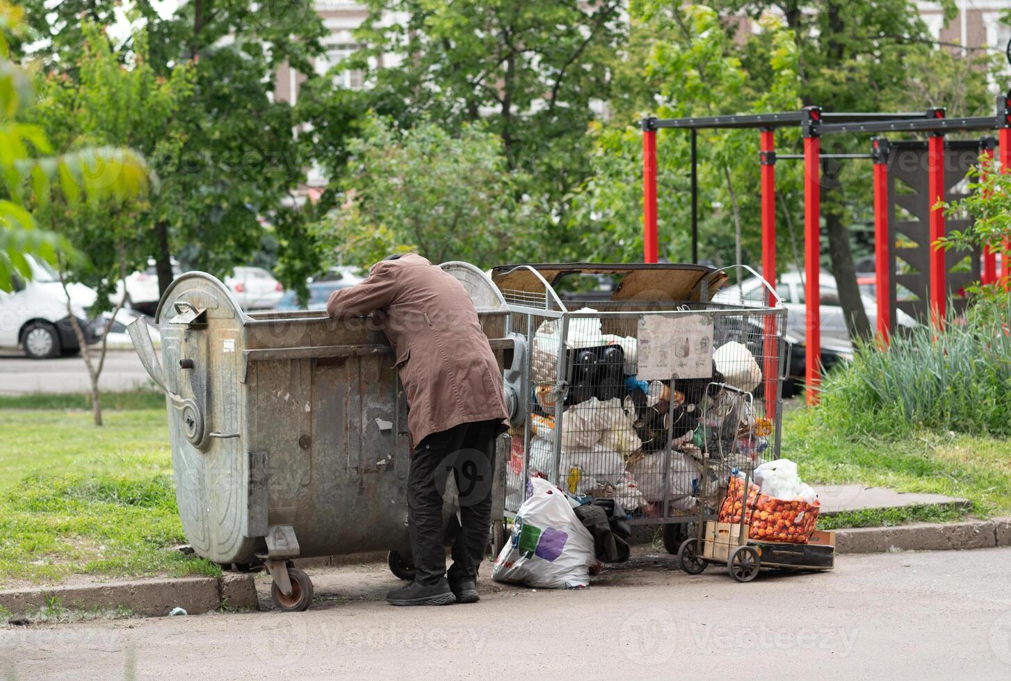 Hungry Man rummaging in trash container bin. Starving man looking for food in household rubbish photo