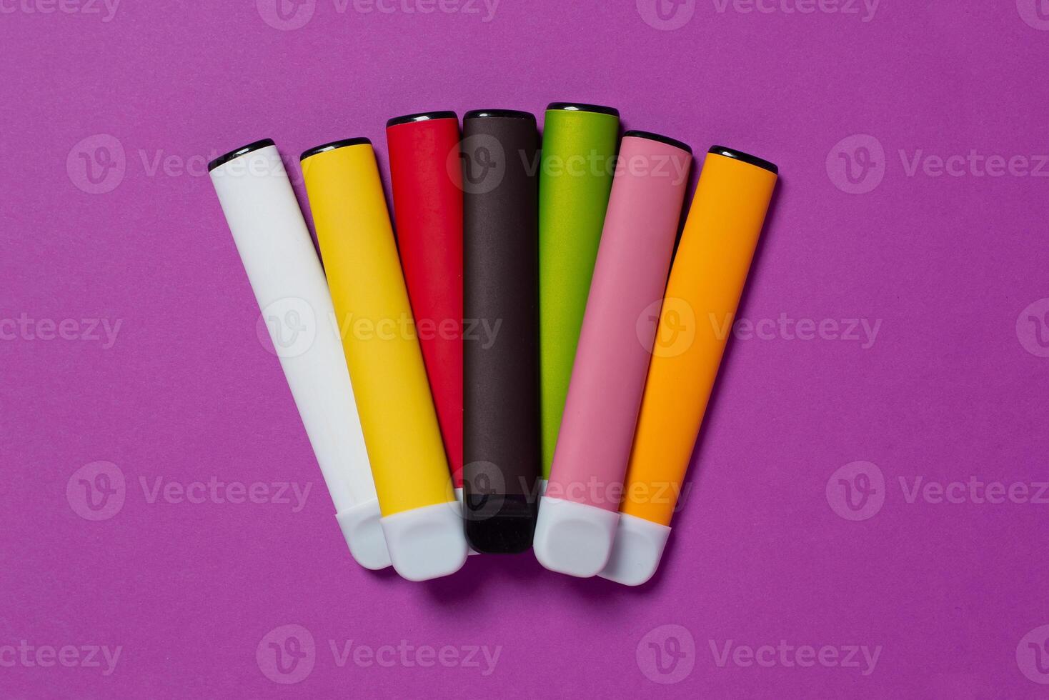 Set of colorful disposable electronic cigarettes on a purple background. The concept of modern smoking, vaping and nicotine. Top view photo