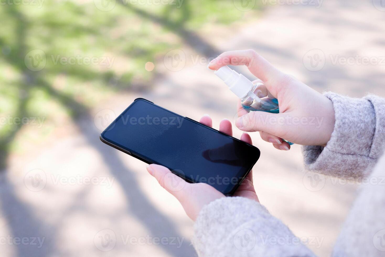 How to clean, sanitize your phone. Cleaning mobile phone to eliminate germs, coronavirus Covid-19. Man hands cleaning smartphone by disinfectant spray.Hygiene concept. photo