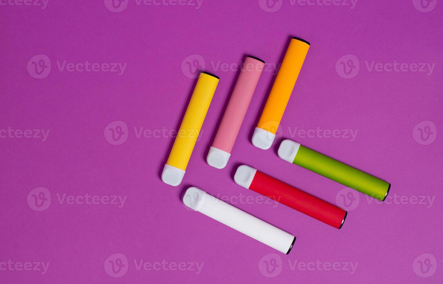 Colorful disposable electronic cigarettes on a purple background. The concept of modern smoking, vaping and nicotine. Top view. photo