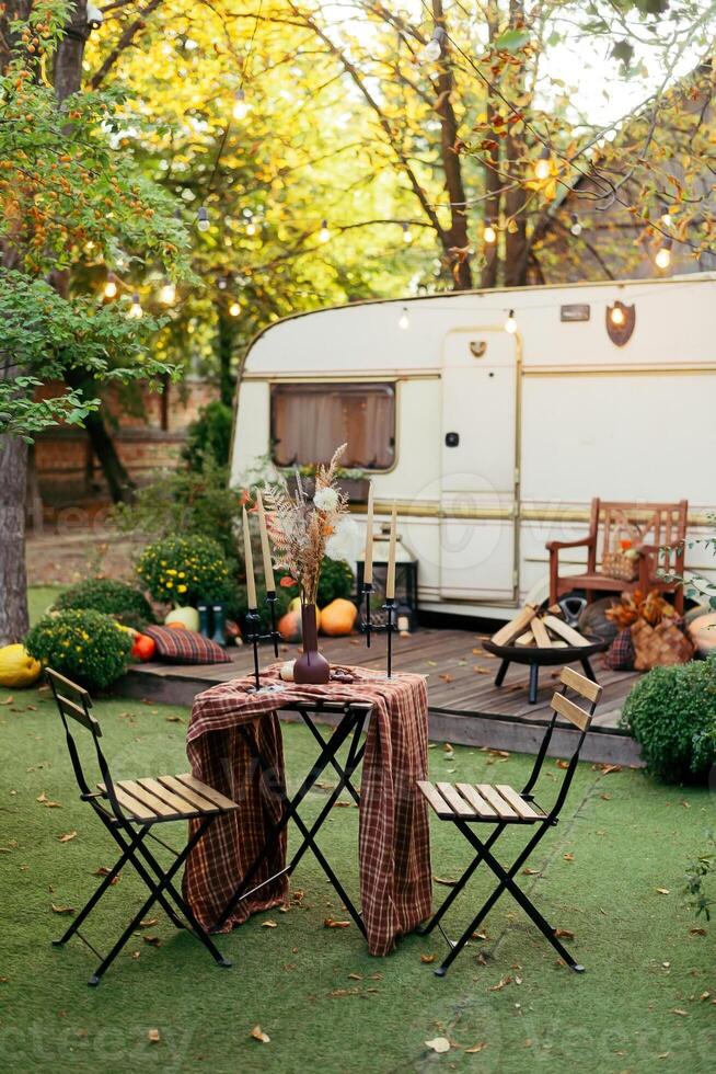 Autumn evening, romantic dinner in the garden. Table with tablecloth and decoration. Trailer with autumn decor and light bulbs photo