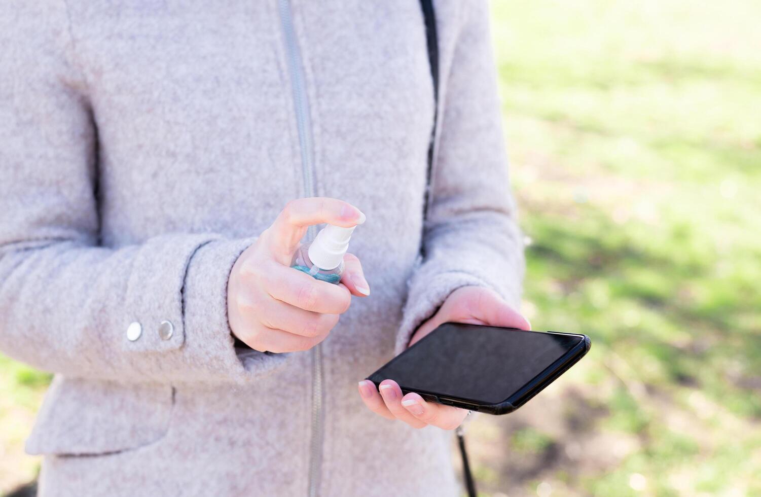 Close up female hand holding smartphone and cleaning spray on her smartphone. Good personal hygiene practices on the street photo