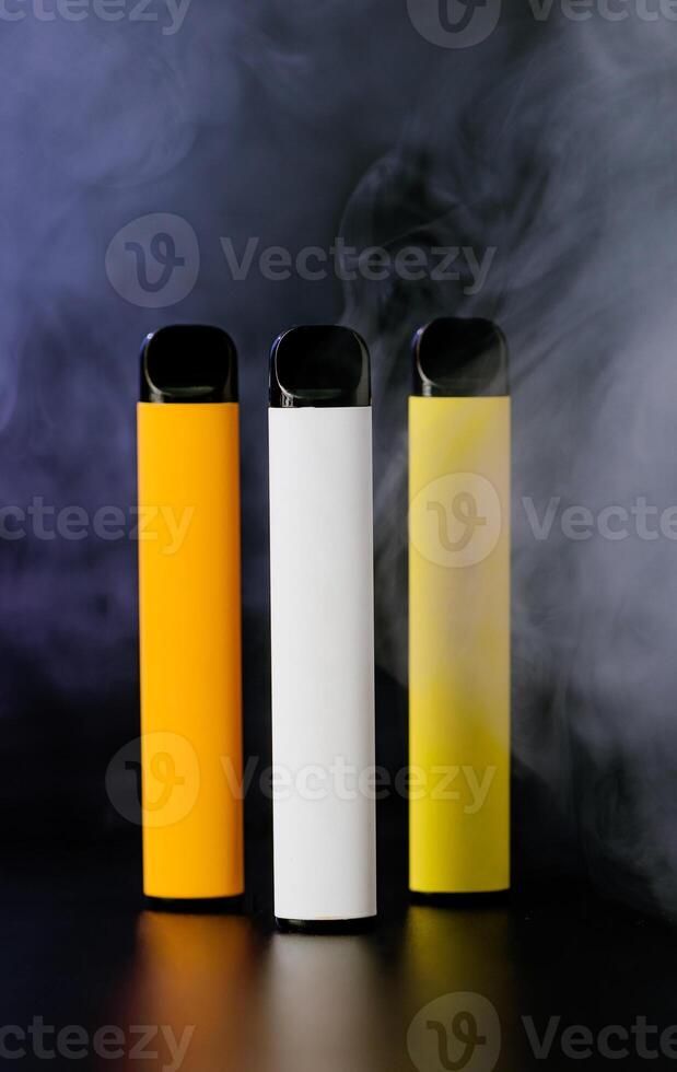 Colorful disposable electronic cigarettes on a black background with smoke. The concept of modern smoking, vaping and nicotine. photo