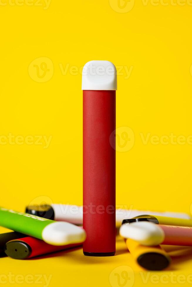 Colorful disposable electronic cigarettes on a yellow background. The concept of modern smoking, vaping and nicotine. photo
