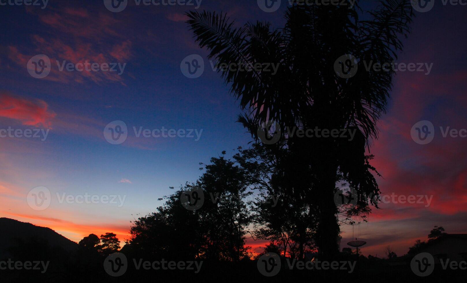 The sunrises in a mountain with silhouettes of hills and several trees that usually grow in tropical rainforests photo