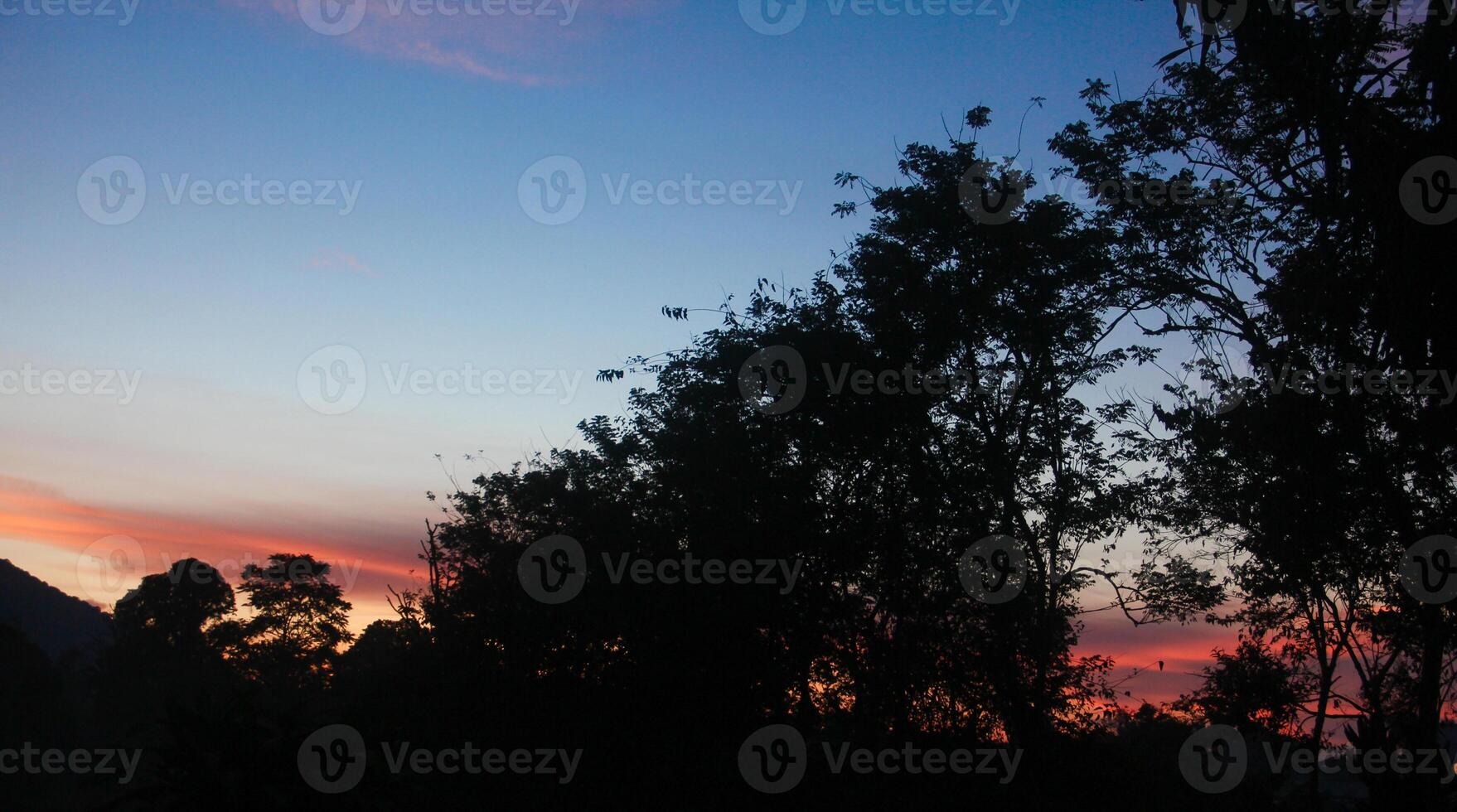The sunrises in a mountain with silhouettes of hills and several trees that usually grow in tropical rainforests photo
