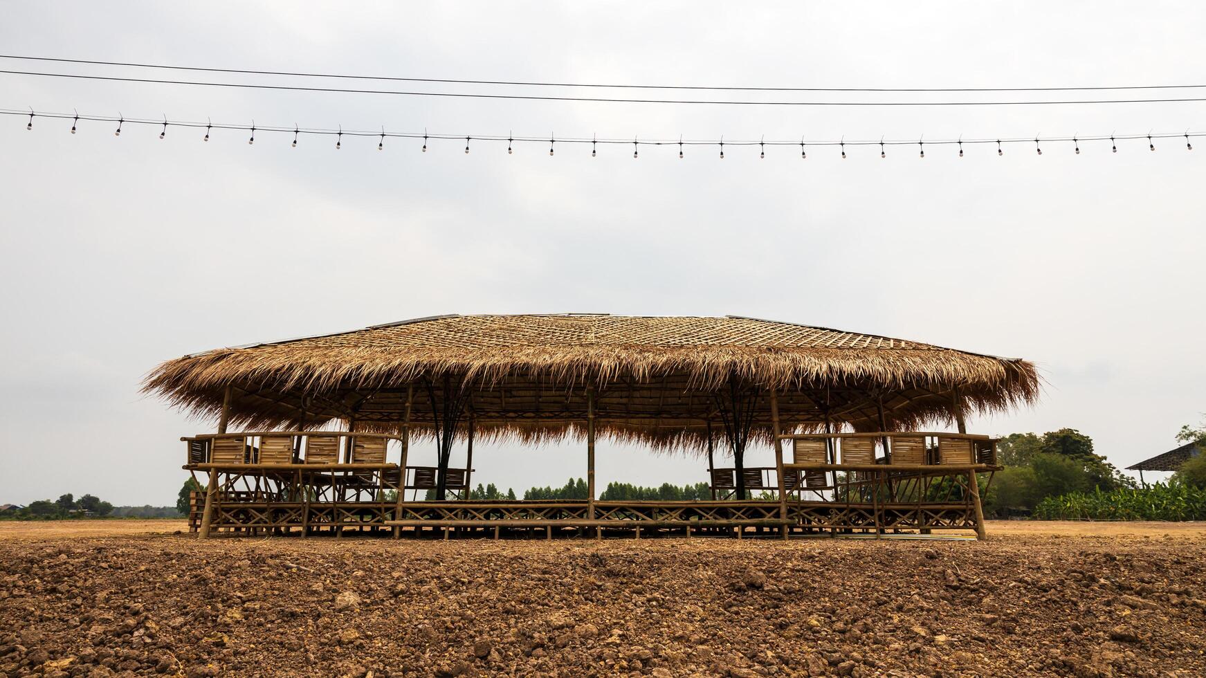 A view of a large bamboo-roofed chair shelter pavilion installed on a mound to shelter. photo