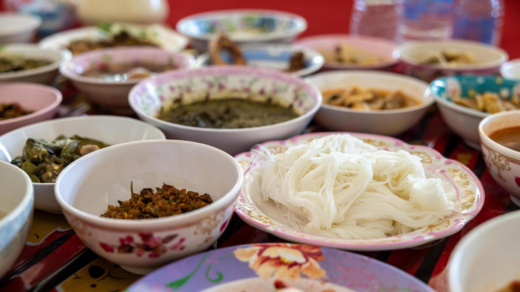 A close-up view of khanom jeen, curry, fried eggs, stir-fries and many other dishes packed in bowls. photo
