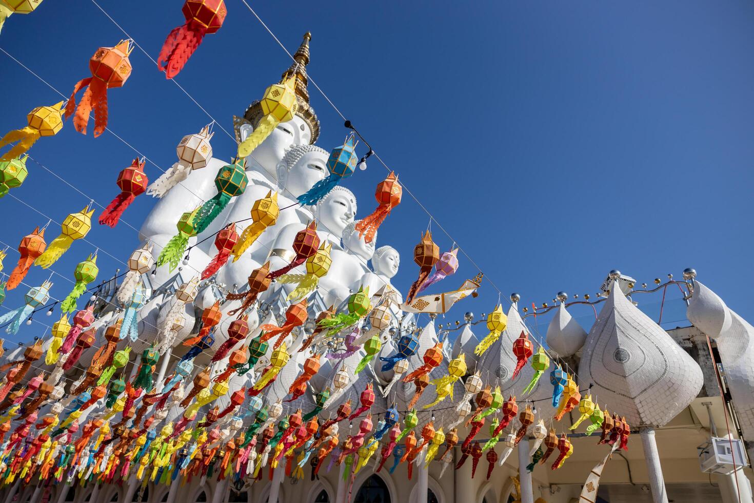 Low-rise view through a tangle of colorful flags hanging near a large, towering colored Buddha statue. photo