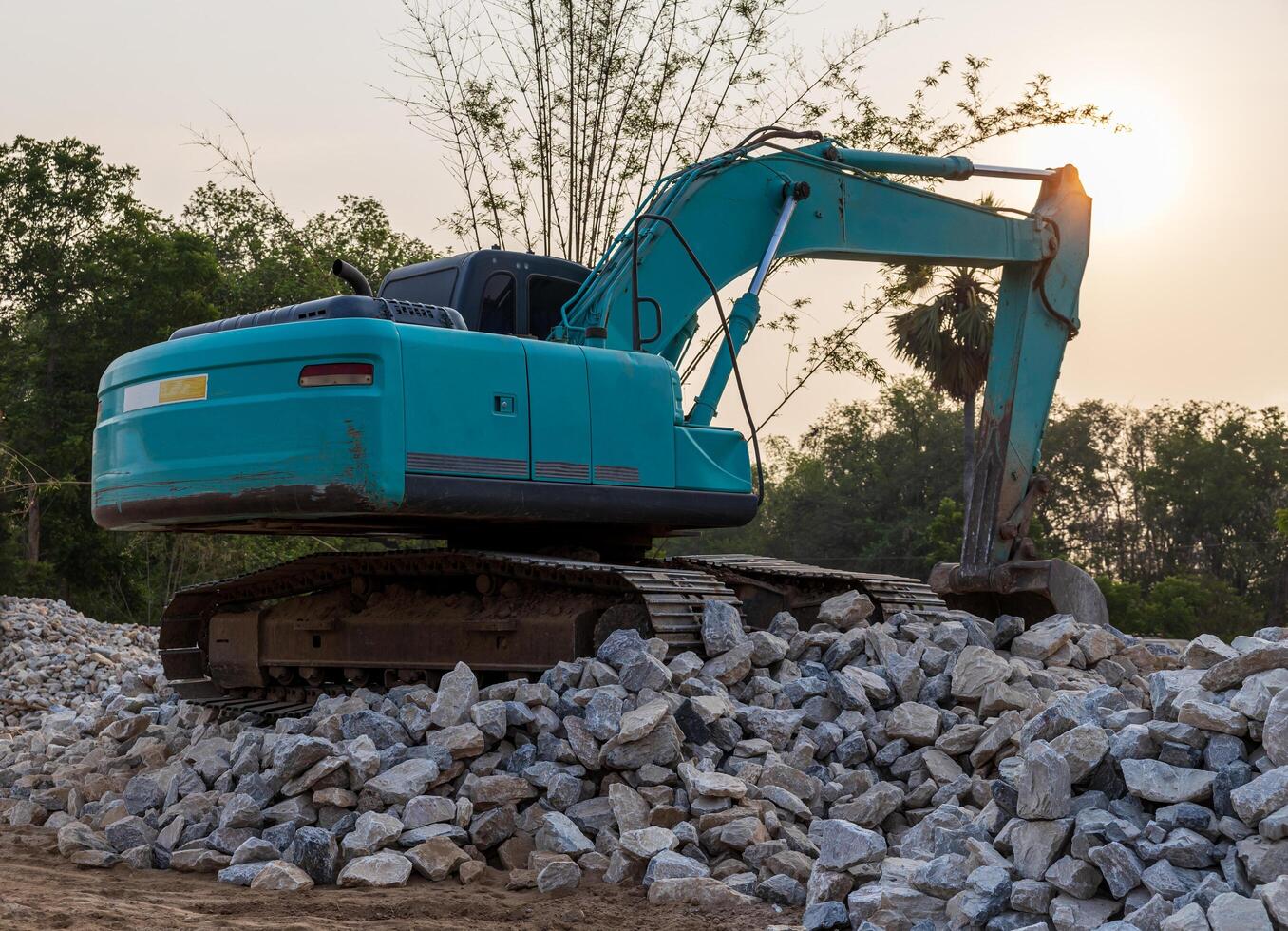 A low-angle view of a green backhoe parked on a pile of granite rubble. photo