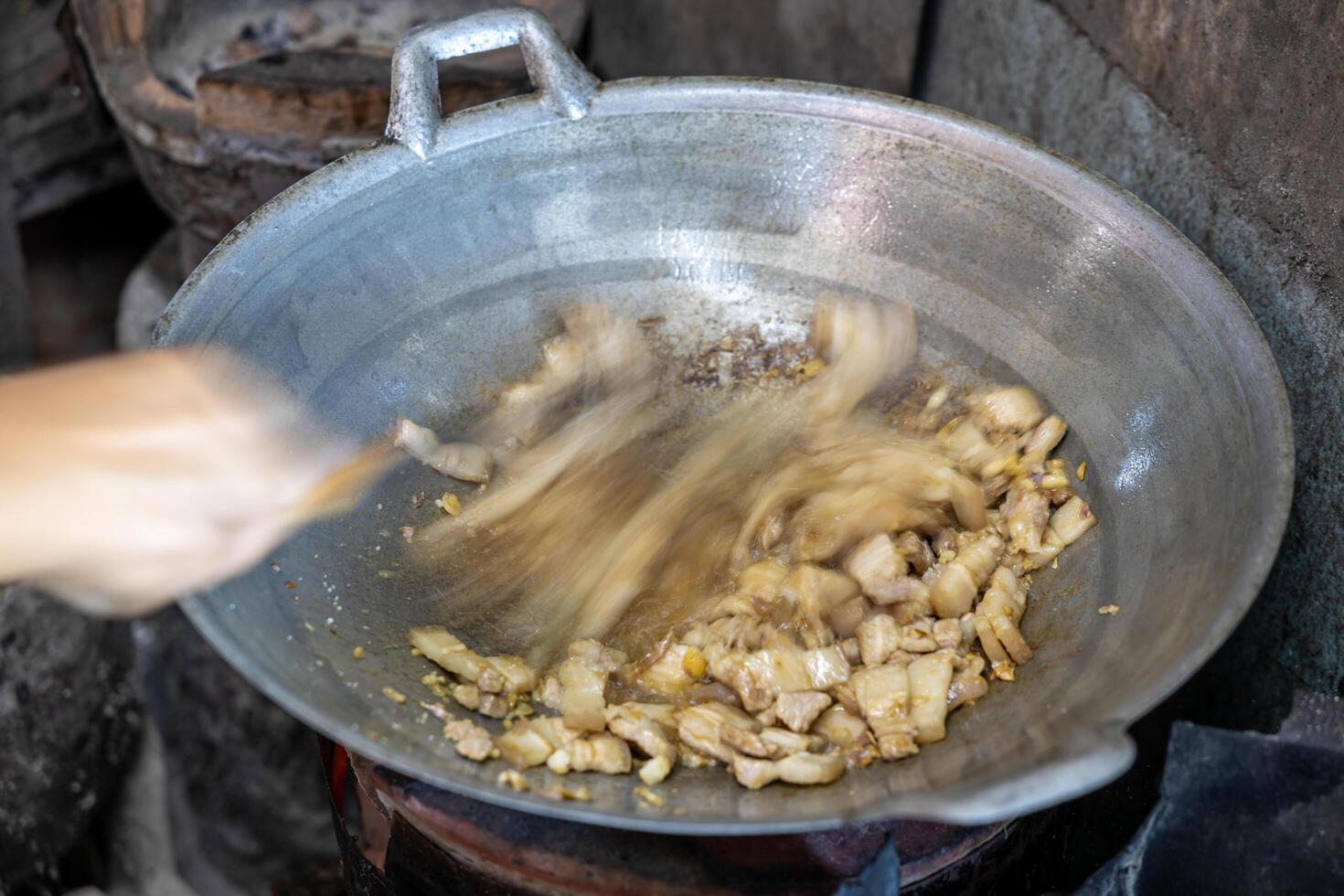Close-up view of blurred motion of a female cook's hand holding a spatula to stir-fry pork. photo
