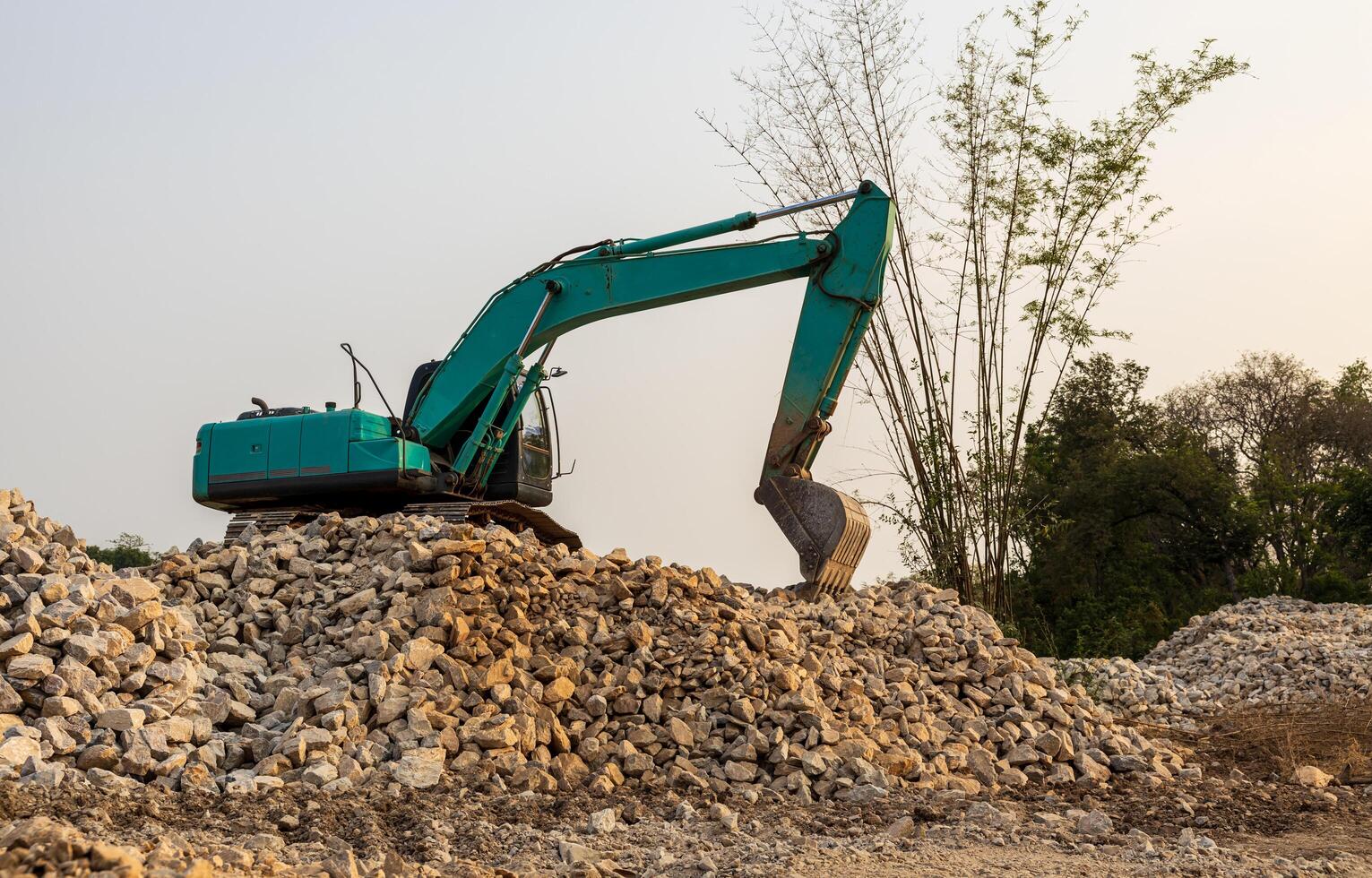 A low-angle view of a green backhoe parked on a pile of granite rubble. photo