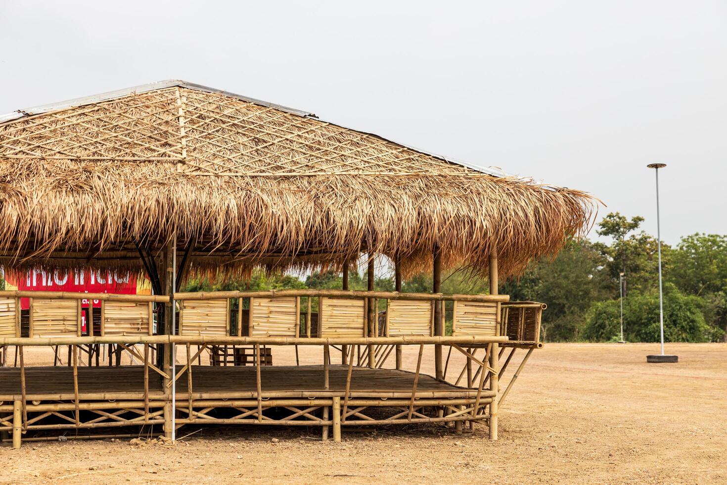 A view of a large bamboo-roofed chair shelter pavilion installed on a mound to shelter. photo