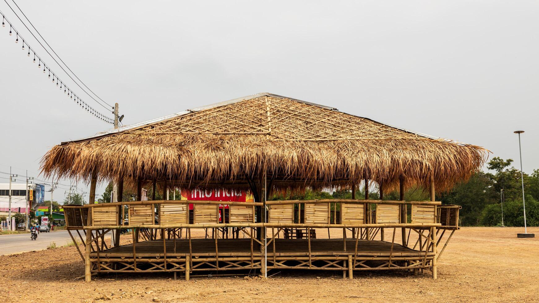 A view of a large bamboo-roofed chair shelter pavilion installed on a mound to shelter. photo