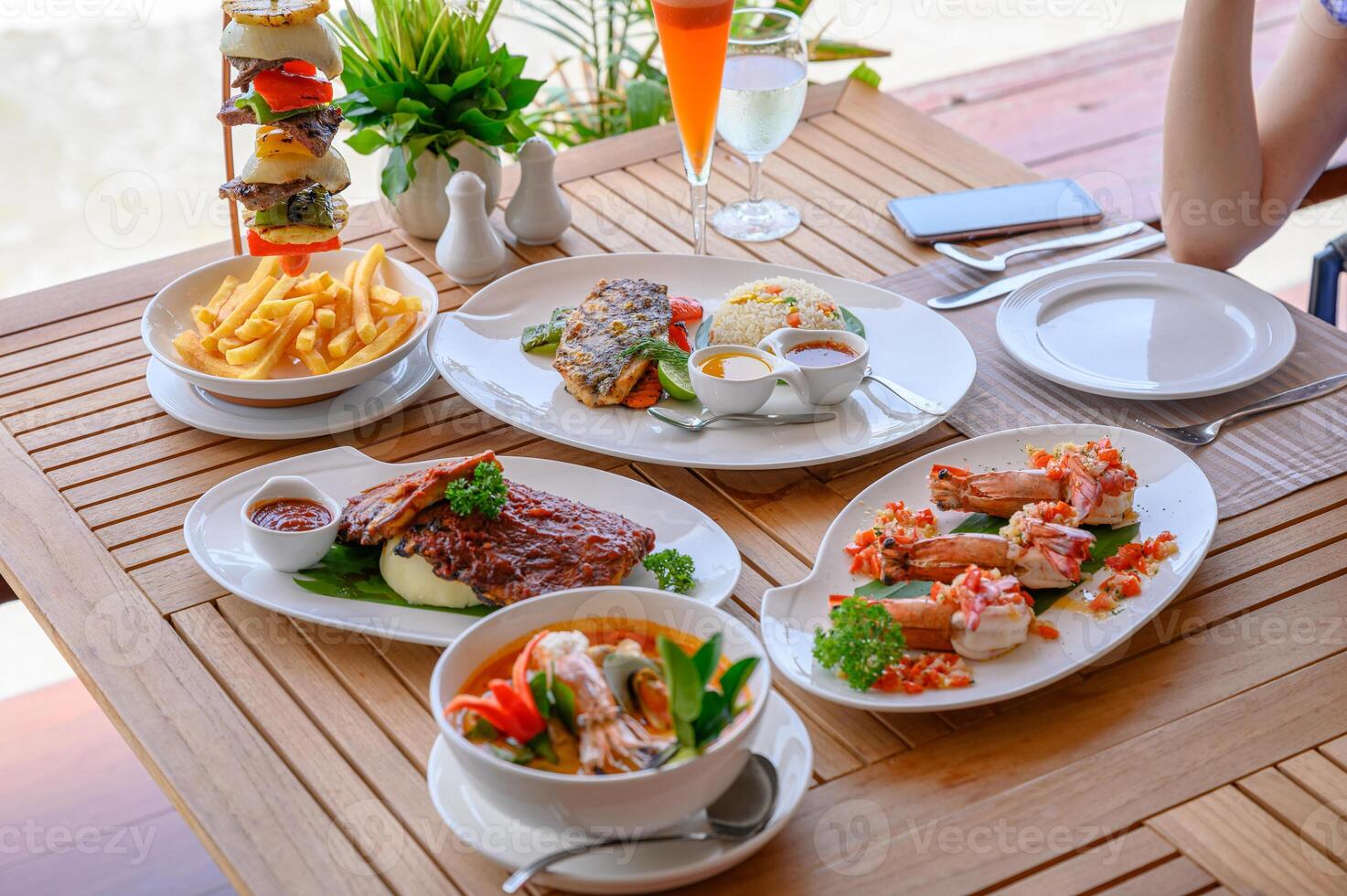 Variety of food, roasted pork ribs, beef steak, seafood and spicy soup on dining table photo