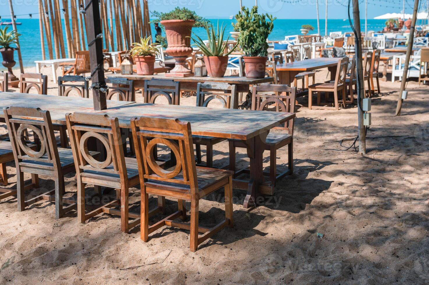 Celebration venue with wooden long table, chair, light bulb hanging and plant decoration in retro style on the beach photo