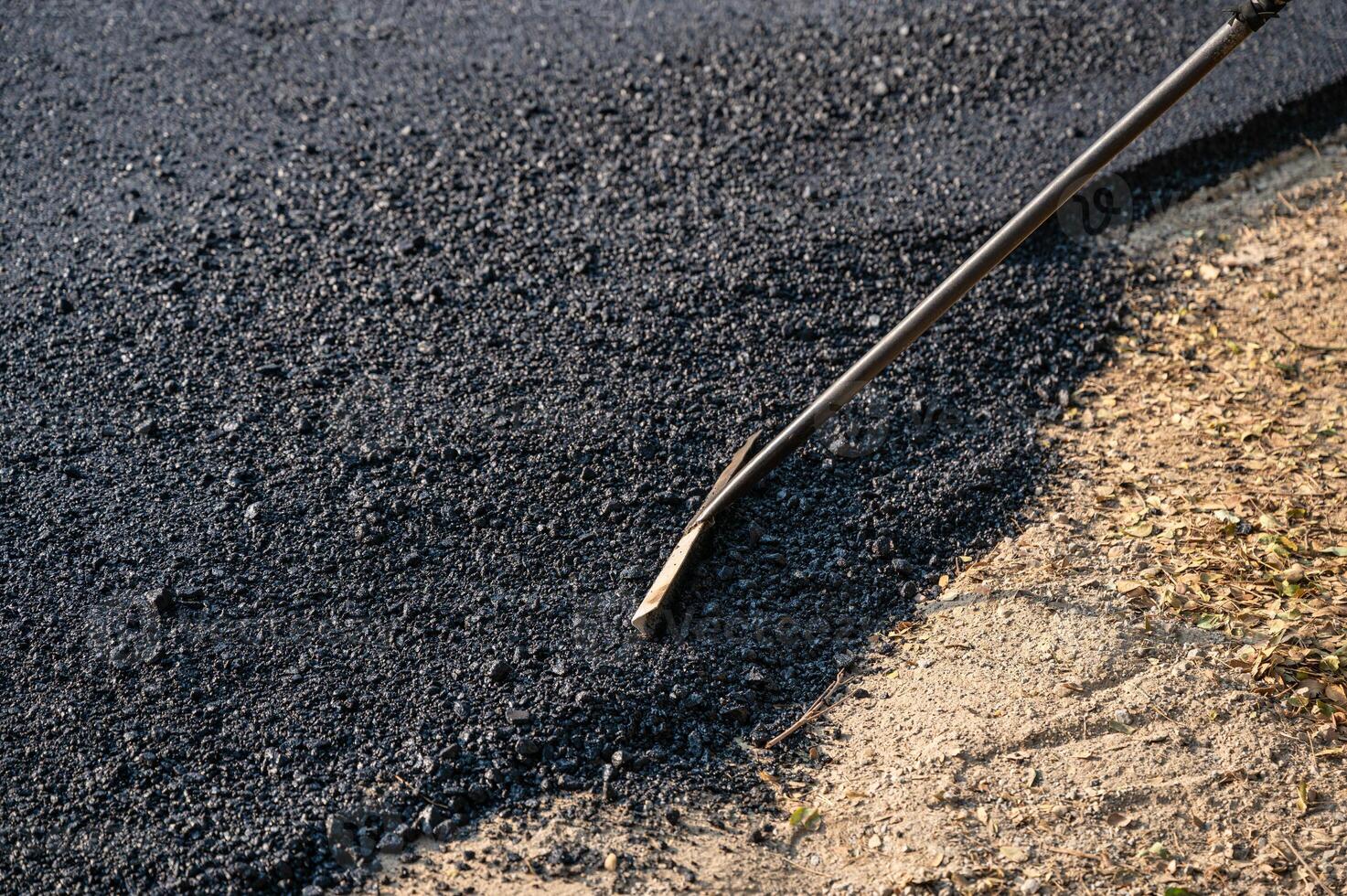 Construction worker using tool spread the hot-mix asphalt road accurately level covering on highway photo