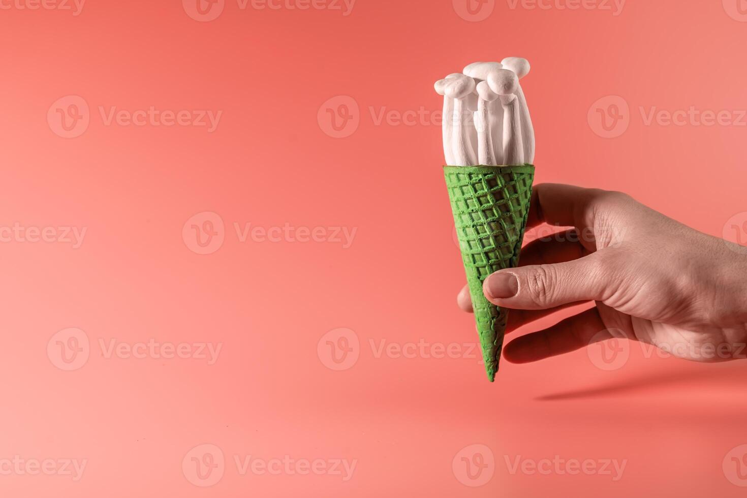 hand holding shimeji mushrooms in an ice cream cone, on bright, colorful, pink background photo